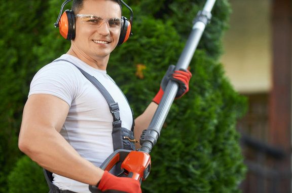 Man with a vertical grass trimmer and a bush behind him